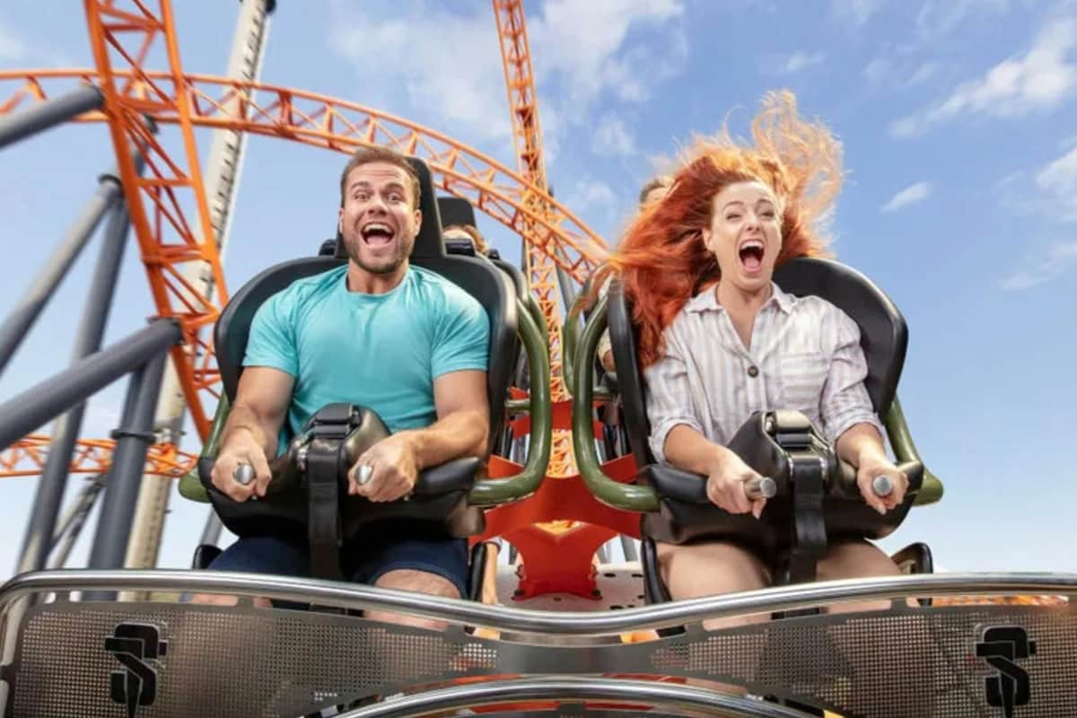 Dreamworld, SkyPoint & WhiteWater World: 5-Day Pass Two people riding a roller coaster with orange tracks under a blue sky; one is visibly excited.