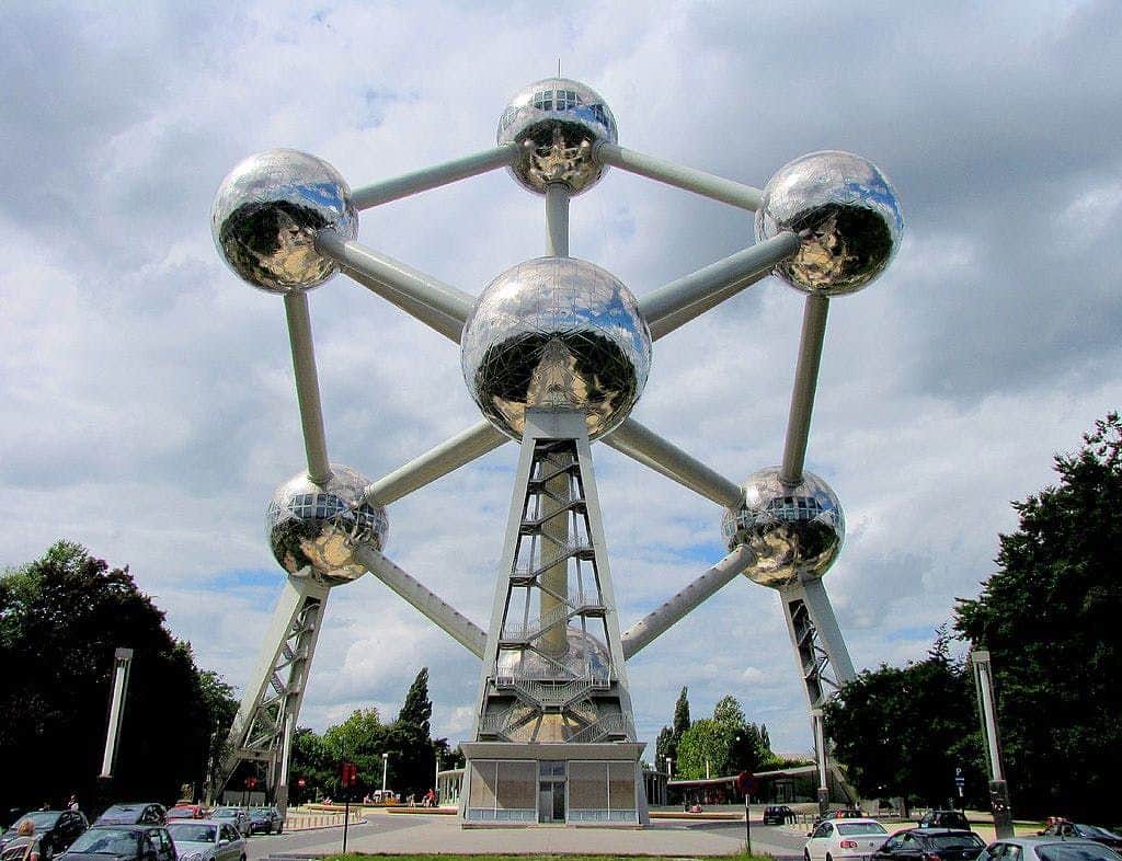 Atomium & Design Museum: Admission Ticket A large steel structure featuring interconnected spheres with metallic surfaces, set against a cloudy sky. Parking lot and trees around.