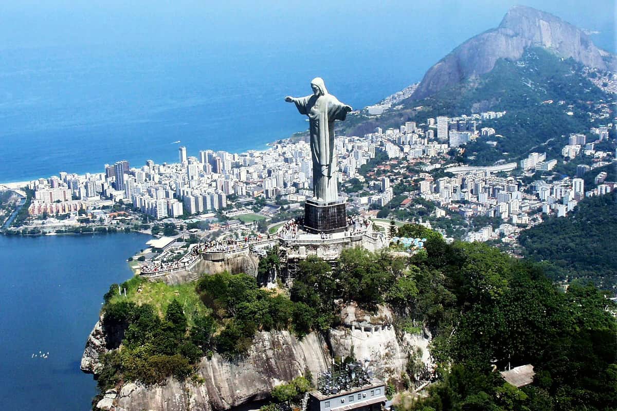 Corcovado Train & Christ the Redeemer Aerial view of Christ the Redeemer statue on a large hill overlooking a cityscape with numerous buildings and a coastline.