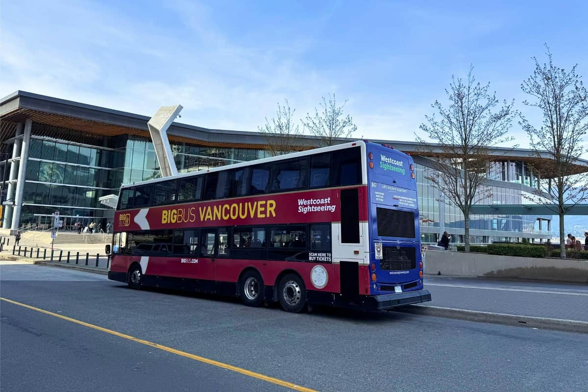 A double-decker tour bus labeled "Big Bus Vancouver" is parked by a modern building on a clear day.