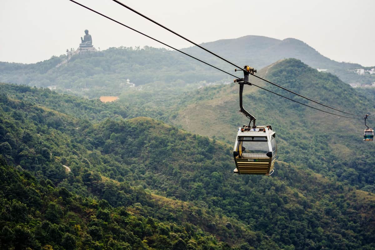 Ngong Ping Cable Car: Standard/Crystal Cabin An empty cable car suspended over a lush mountainous landscape with a large Buddha statue visible in the distance.