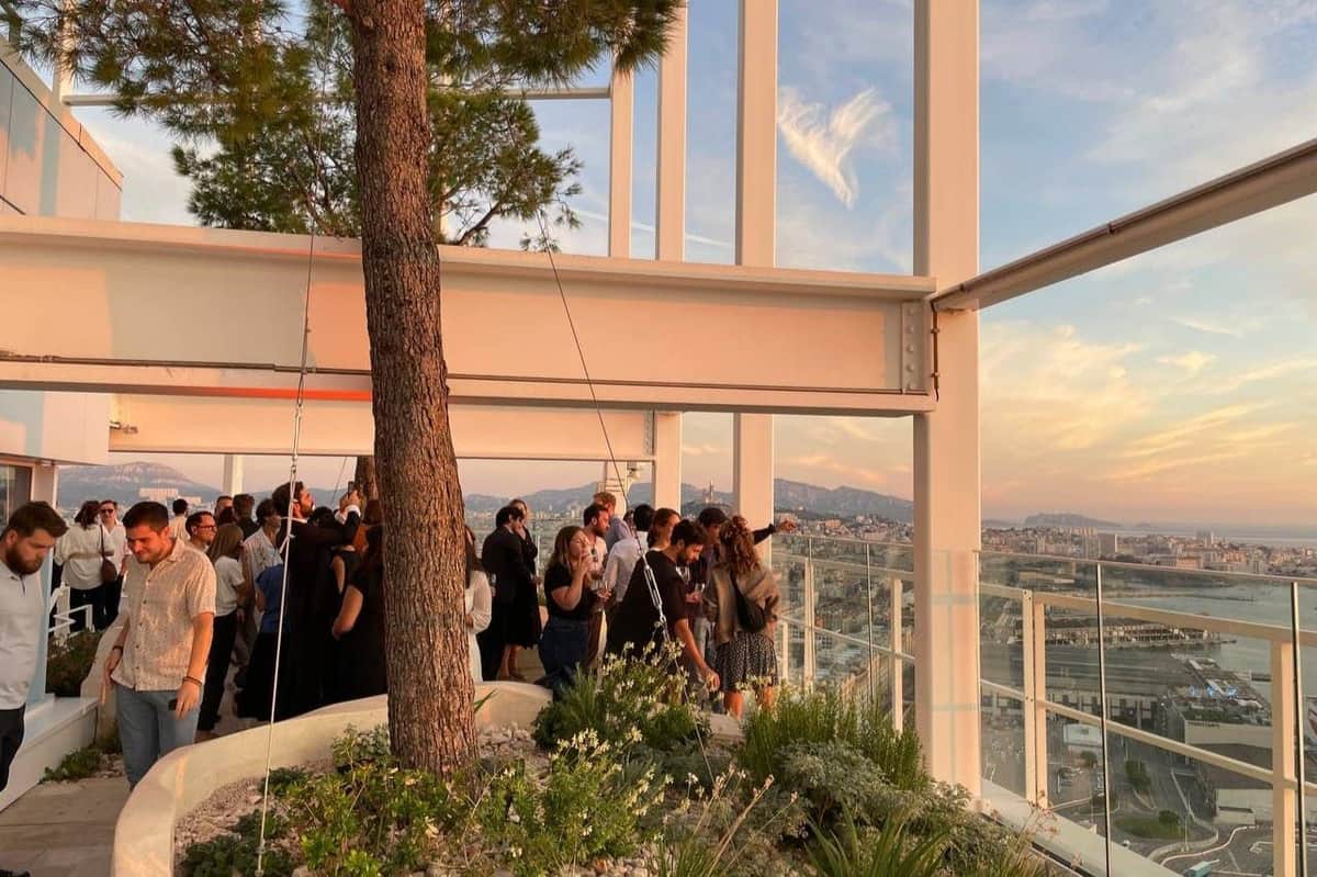 Sky Centre Marseille: 30th Floor Access People mingling at an outdoor gathering with a large tree, modern architecture, and scenic city view in the background.