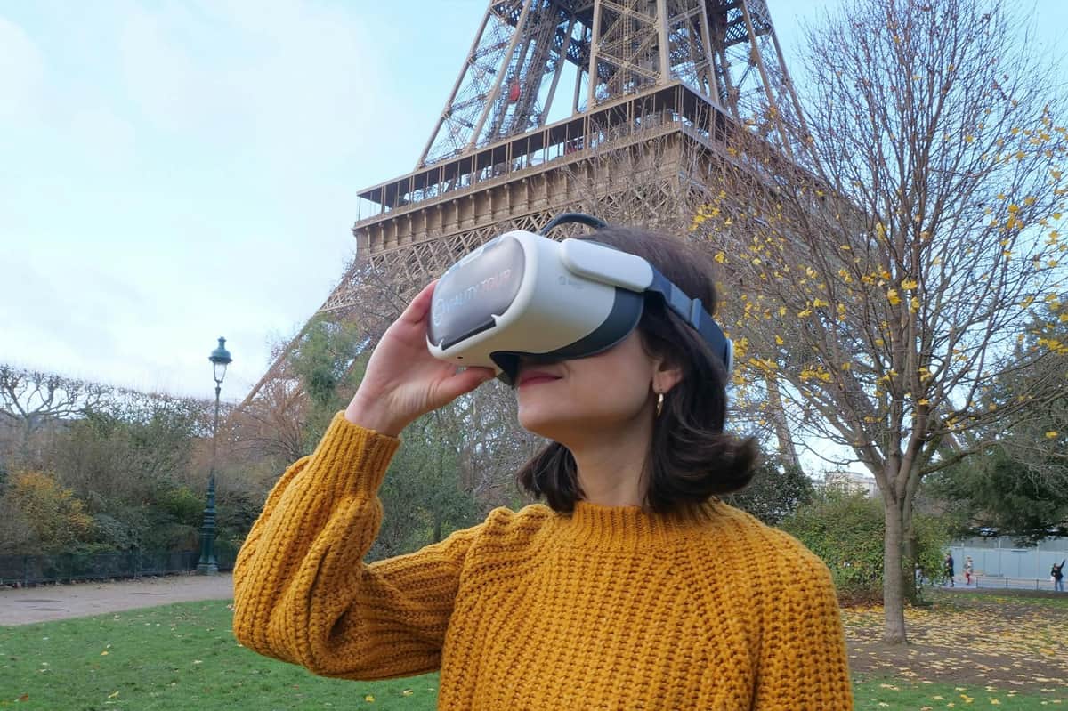 Eiffel Tower: Guided VR Experience A person in a yellow sweater uses a virtual reality headset near the Eiffel Tower in a park setting on a clear day.