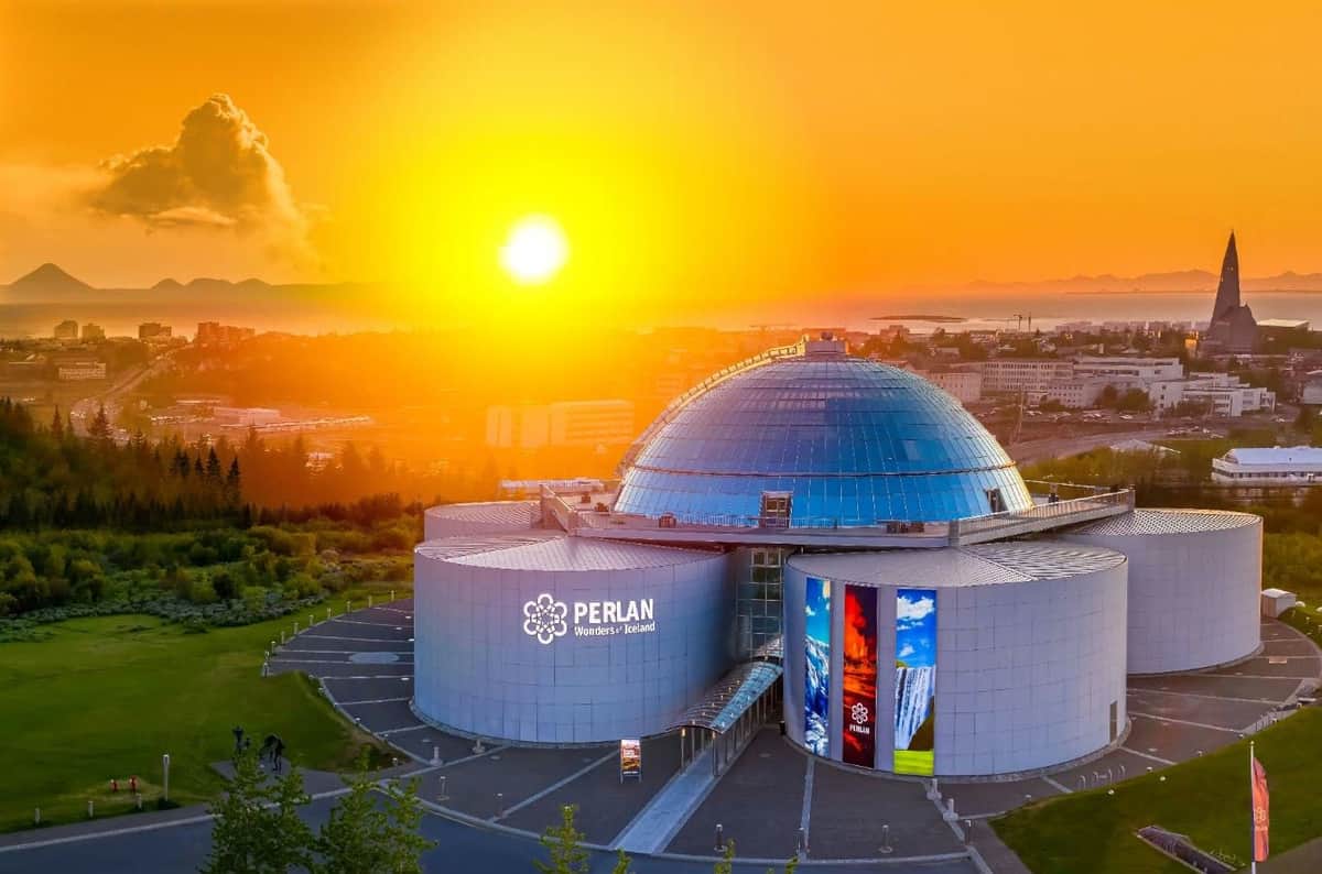 Perlan: Entry Ticket A futuristic glass-domed building labeled 'Perlan Wonders of Iceland' under a vibrant orange sunset with a cityscape in the background.