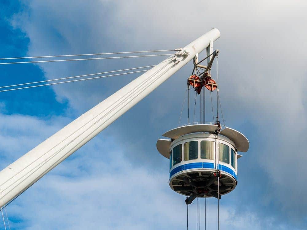 Bigo Panoramic Lift: Fast Track Ticket A round observation deck, with windows, is suspended by cables from a large white crane against a background of blue sky and clouds.