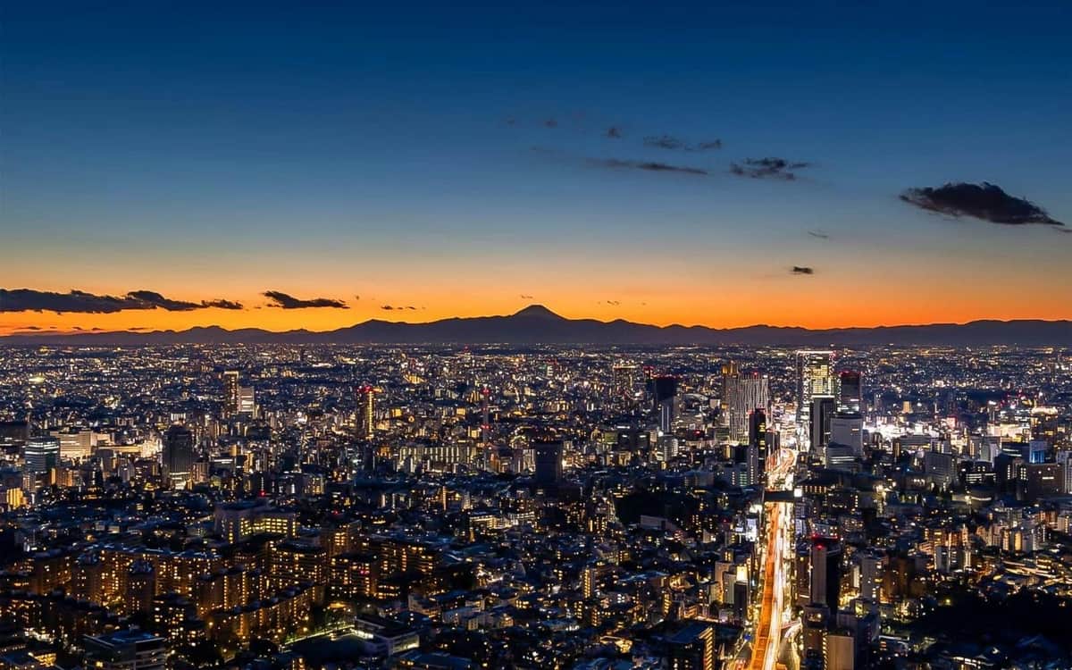 東京:六本木ヒルズシティビュー展望台デッキ2名参加チケット 明るい街の灯りと、オレンジ色の空に映える山のシルエットが背景にある夕暮れ時の街並み。