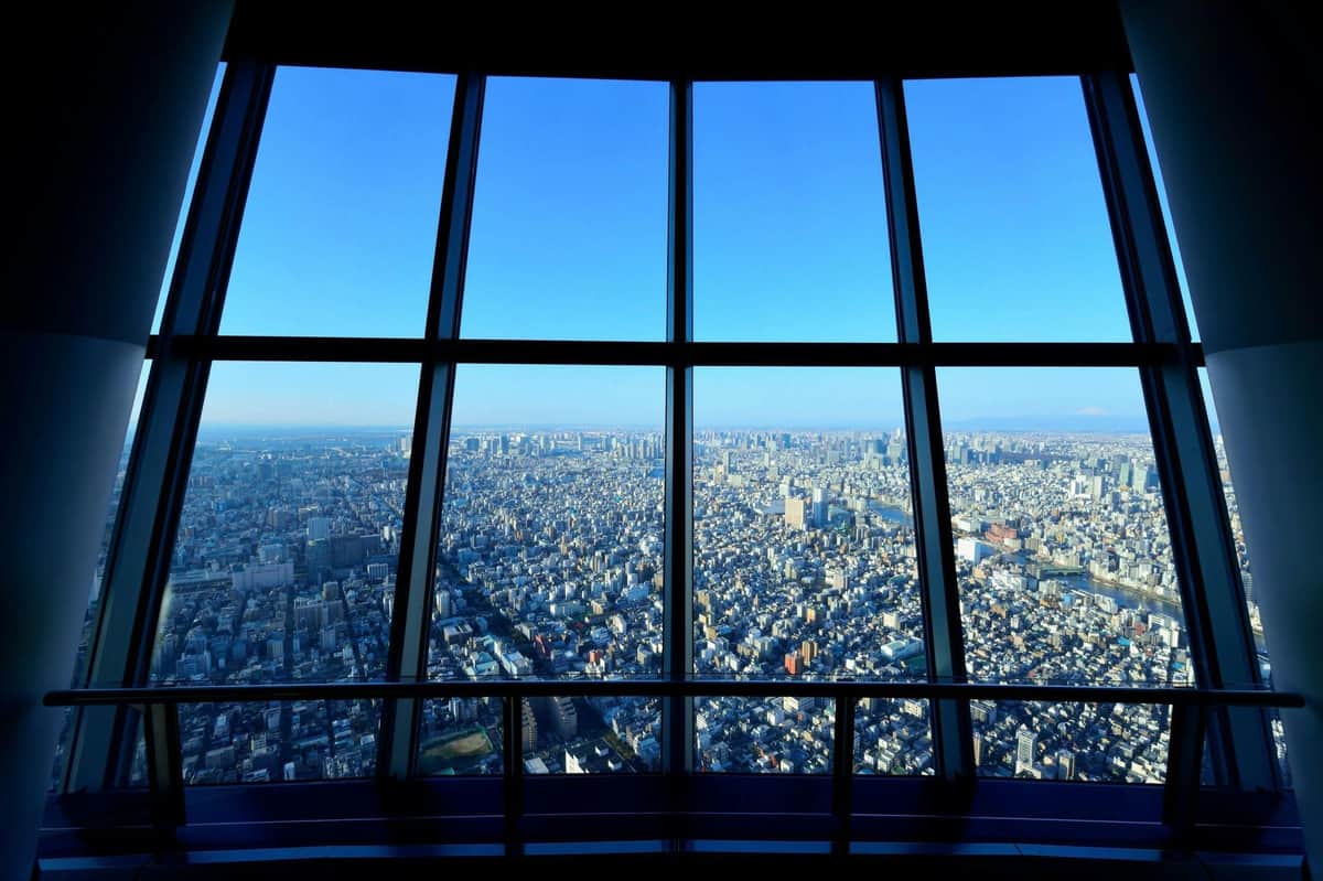 Tokyo Skytree & teamLab Planets: Entry Ticket Aerial view of a densely packed cityscape seen through large windows on a high floor, with a clear blue sky.