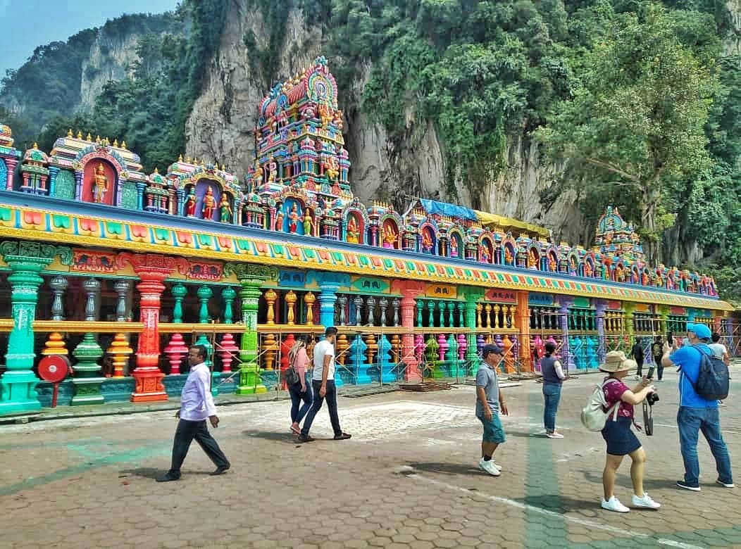 Genting Highlands & Batu Caves: Day Trip from Kuala Lumpur People walking near a vividly colored, ornate temple building against a backdrop of rocky cliffs and lush greenery.