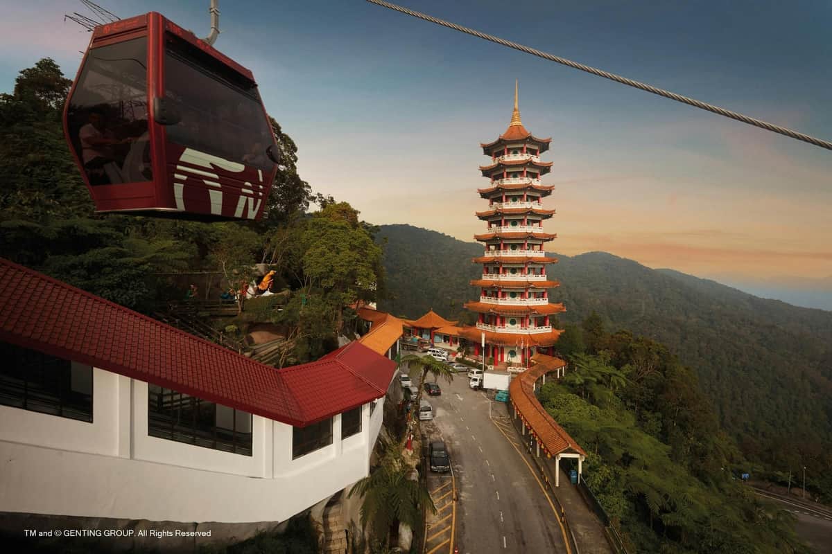 Genting Highlands: bilet na gondolę ze szklaną podłogą - Awana SkyWay One-Way Czerwona kolejka linowa w pobliżu wielopoziomowej pagody na pagórkowatym, zalesionym terenie, z wijącą się przez scenę drogą.
