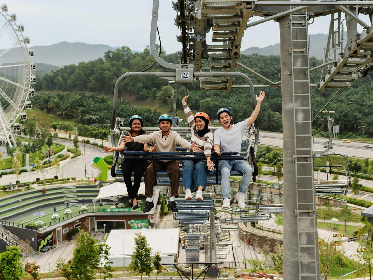 스카이라인 루지 쿠알라룸푸르: 루지 3회 탑승 + 스카이라이드 나무와 기반 시설의 경치 좋은 배경을 배경으로 4명이 의자 리프트를 타고 미소를 지으며 손을 흔들고 있습니다.