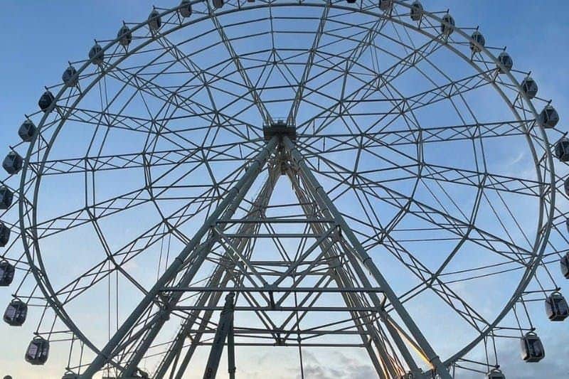 Large Ferris wheel structure with metal framework under a clear blue sky.