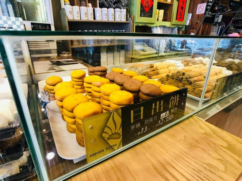 Área Recreativa Forestal Nacional de Alishan: Entrada + Billete de ida y vuelta en la línea de Alishan de Taiwan Good Bus Una vitrina de panadería con montones de bollos amarillos y marrones, etiquetados con el precio y un logotipo.
