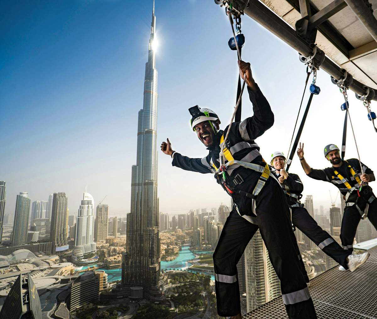 Sky Views Observatory: Entry Ticket + Edge Walk Experience Three people in harnesses pose and smile on an outdoor platform with the Burj Khalifa and Dubai skyline in the background.