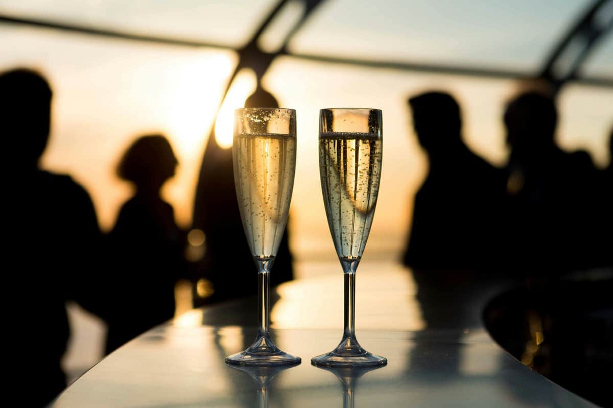 Brighton i360: Sky Bar 360 + Glass of Champagne Two champagne flutes on a table with sunset-lit silhouettes of people in the background.