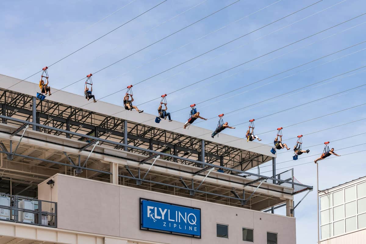 Fly LINQ Zipline Las Vegas: Entry Ticket People ziplining above a building with a sign that reads "Fly LINQ Zipline" and a clear blue sky in the background.