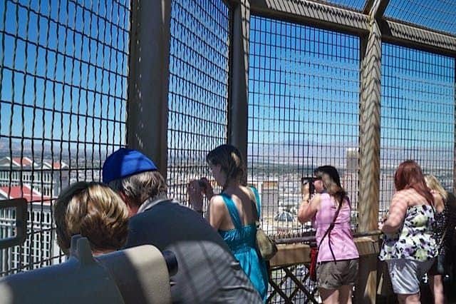 The Eiffel Tower Experience Las Vegas: Entry Ticket People looking through binoculars and taking photos from a high fenced observation deck on a sunny day.