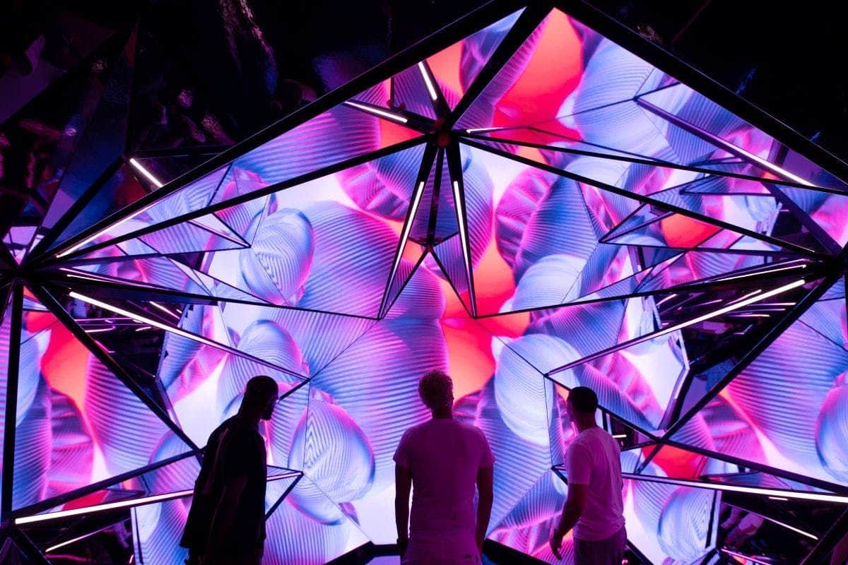 Edge NYC: Express Pass Three people stand in front of a vibrant geometric light installation featuring vivid pink and purple hues.