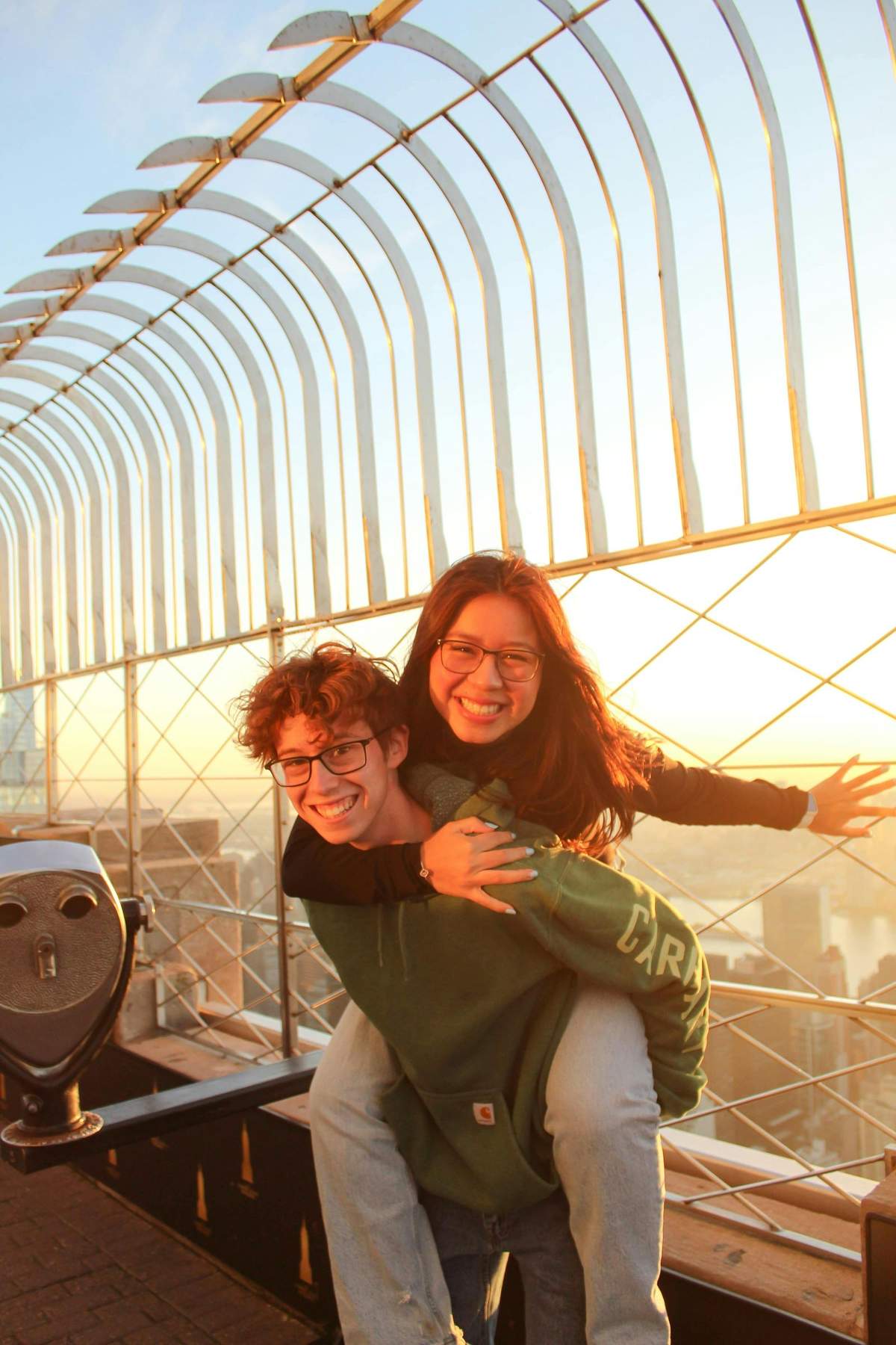 Empire State Building: Sunrise Experience Two people smiling at sunset on a viewing platform, with one giving a piggyback ride and cityscape visible in the background.