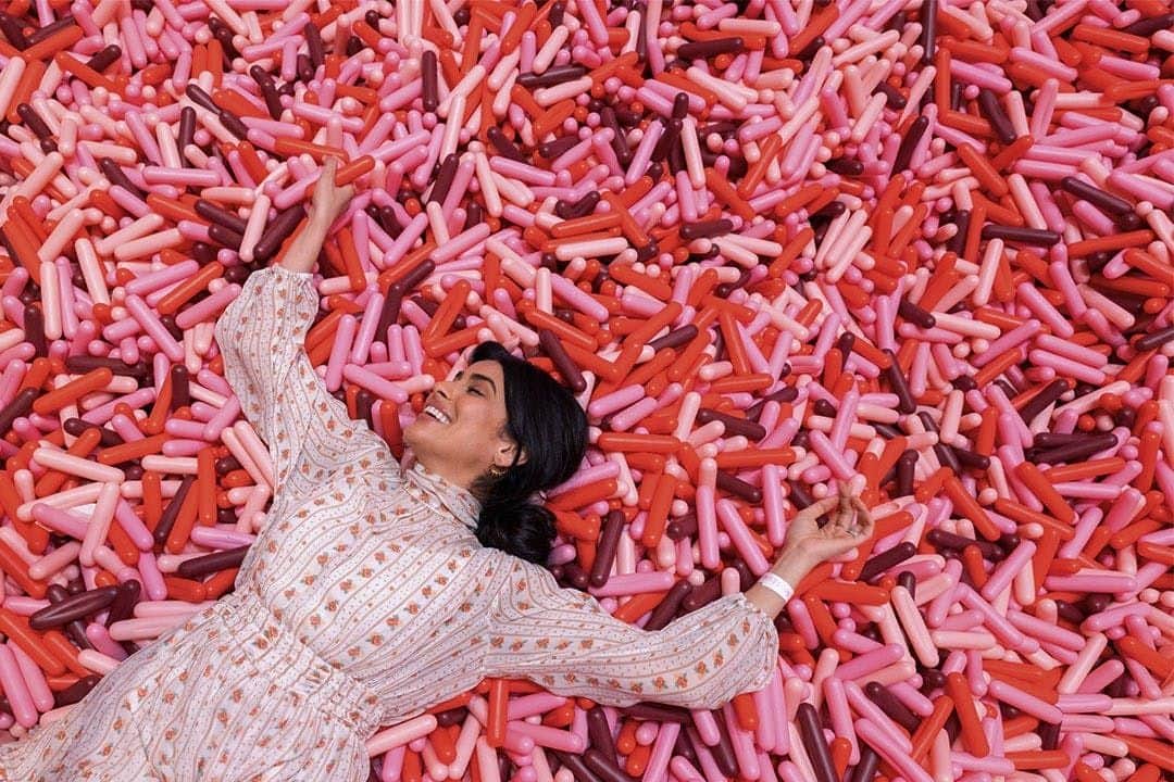 New York: Museum of Ice Cream + One World Observatory A woman in a patterned dress lies on her back, smiling, surrounded by an array of pink, red, and purple balloon-like objects.