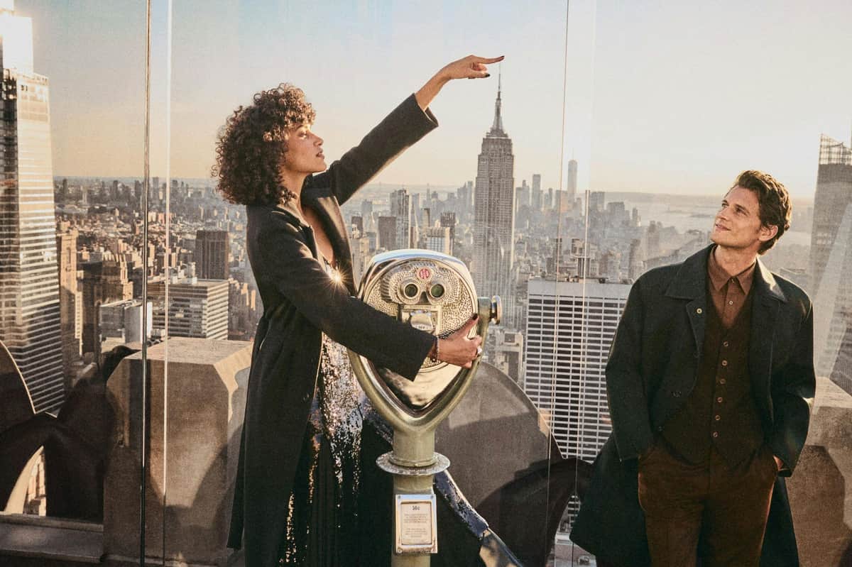 Top of the Rock: All-Inclusive Pass A woman and a man stand on an observation deck overlooking a city skyline, with a viewing telescope in the foreground.