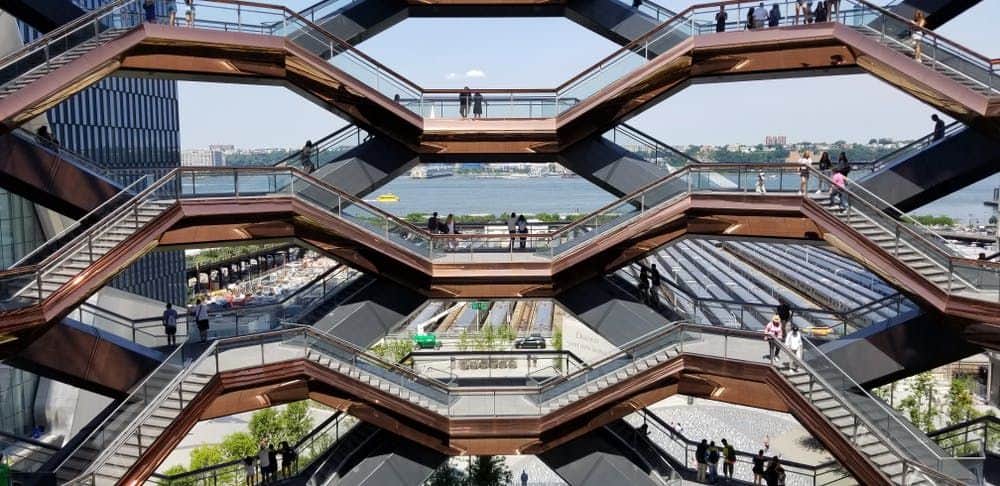 Vessel at Hudson Yards Multi-level structure with people on walkways, river and building in the background, and construction site below.