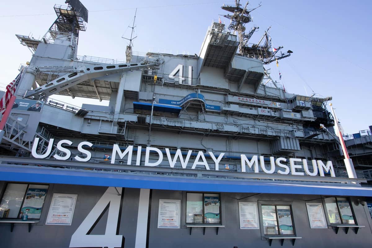 Exterior of the USS Midway Museum ship with large "41" and "USS Midway Museum" text, control towers, and multiple windows visible.