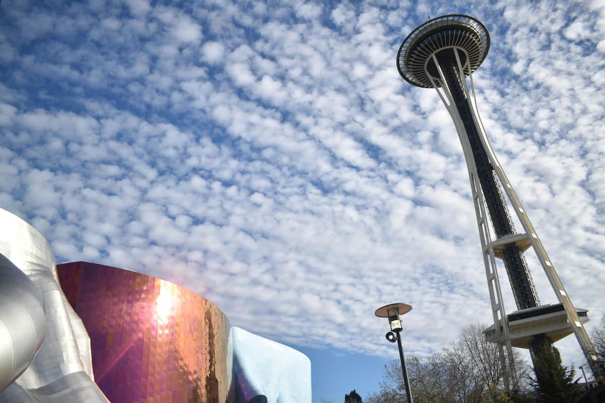 Seattle Center & Space Needle: Guided Walking Tour The image shows the Space Needle, a lamp post, and a reflective, curved building under a partly cloudy sky.