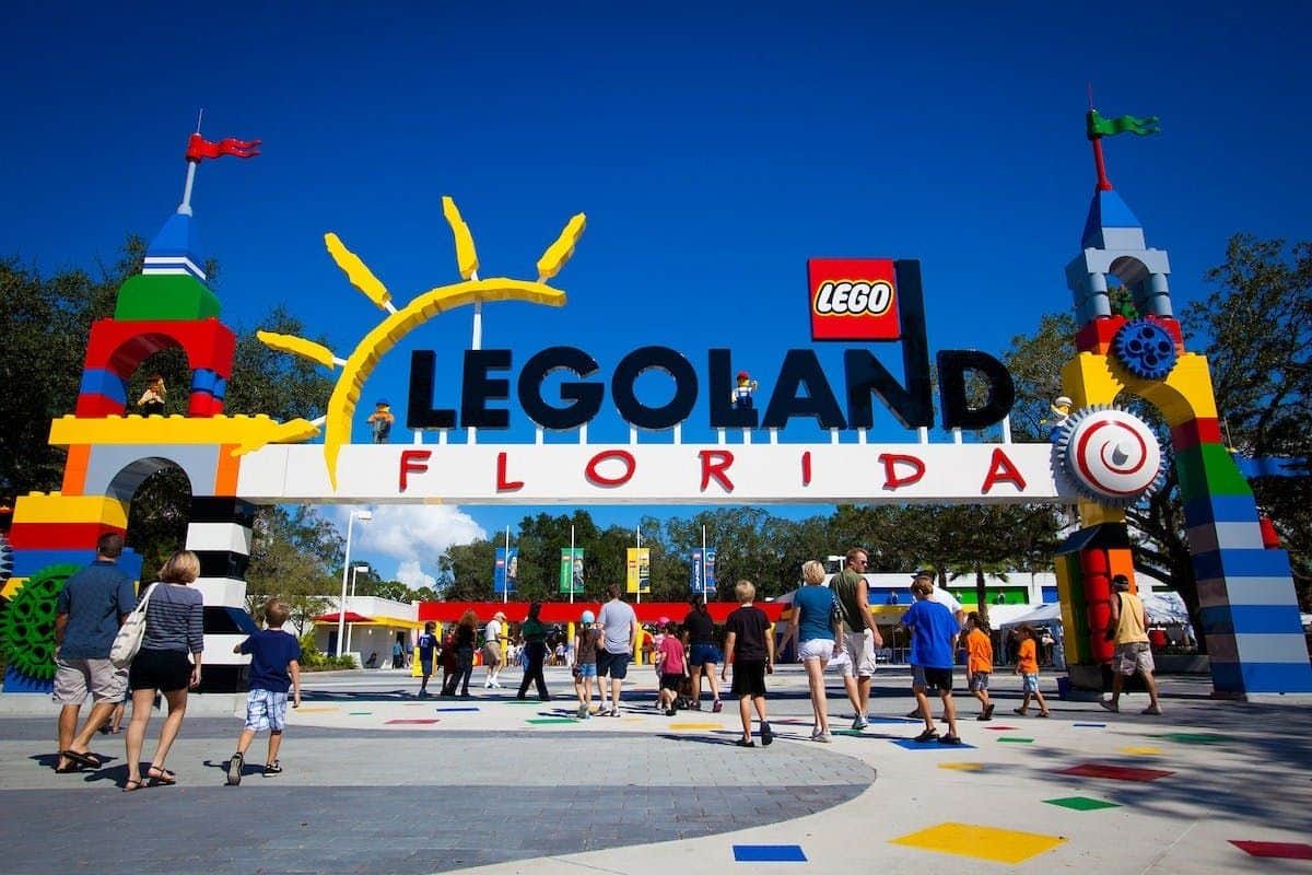 The Florida Pass Entrance to LEGOLAND Florida with colorful decorations and visitors walking around under a sunny blue sky.