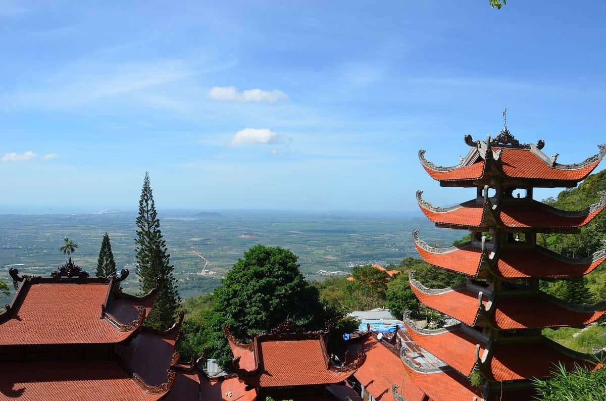 Teleférico TTC World Ta Cu: Bilhete de entrada Uma vista panorâmica de telhados em forma de pagode com beirais curvos, rodeados por árvores, com vista para uma vasta paisagem verdejante sob um céu azul.
