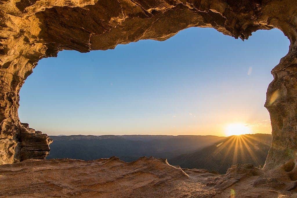 Blue Mountains National Park Rocky cave opening framing a beautiful sunset over distant mountains and a clear sky.