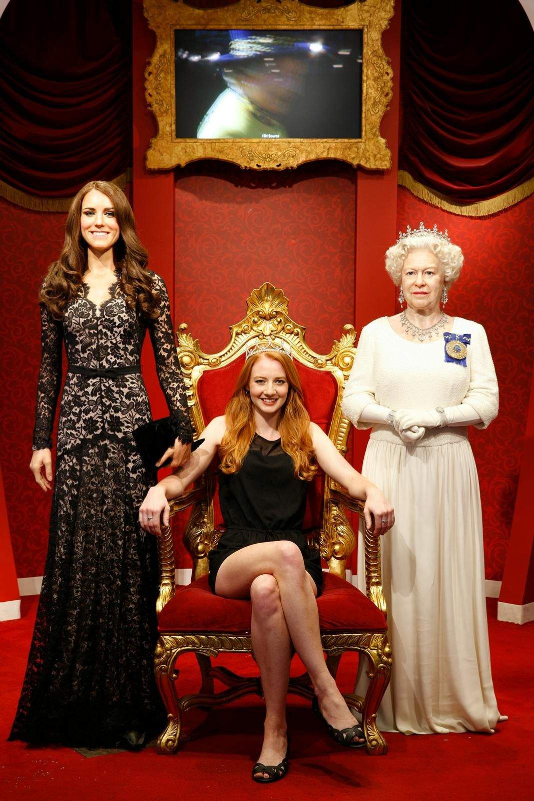 Madame Tussauds Sydney A woman sits on a throne, flanked by two wax figures of women in elegant dresses, against a red backdrop with a framed screen above.