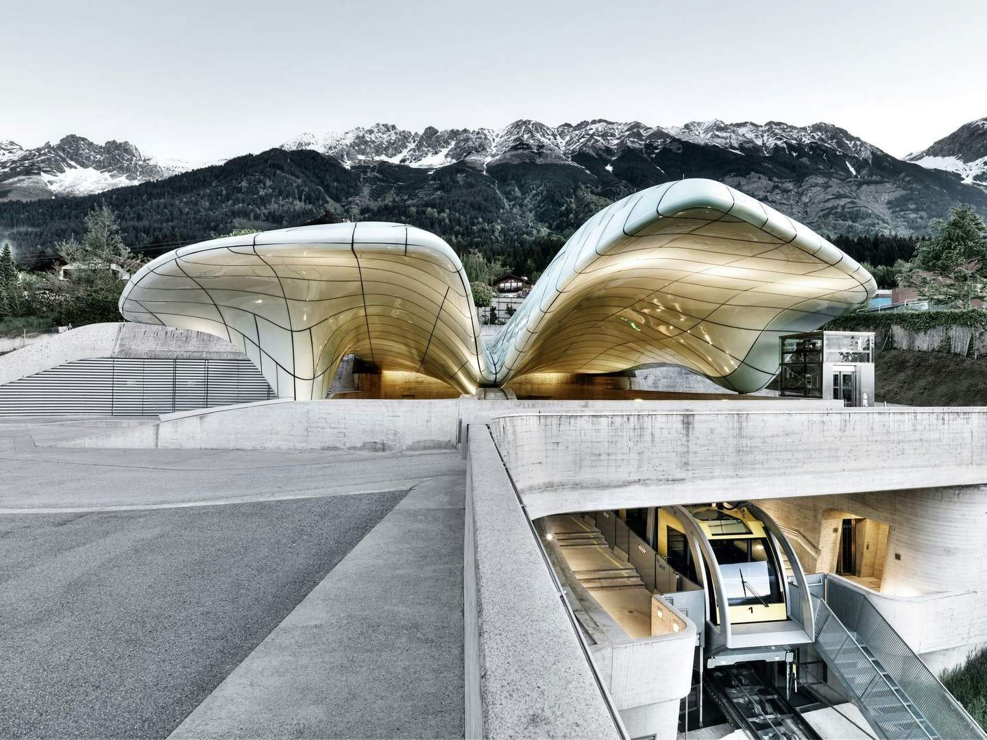 Innsbrucker Nordkettenbahnen - Nordkette Modern architectural structure with a curving, glass canopy and a funicular railway entrance beneath, set against a mountainous backdrop.
