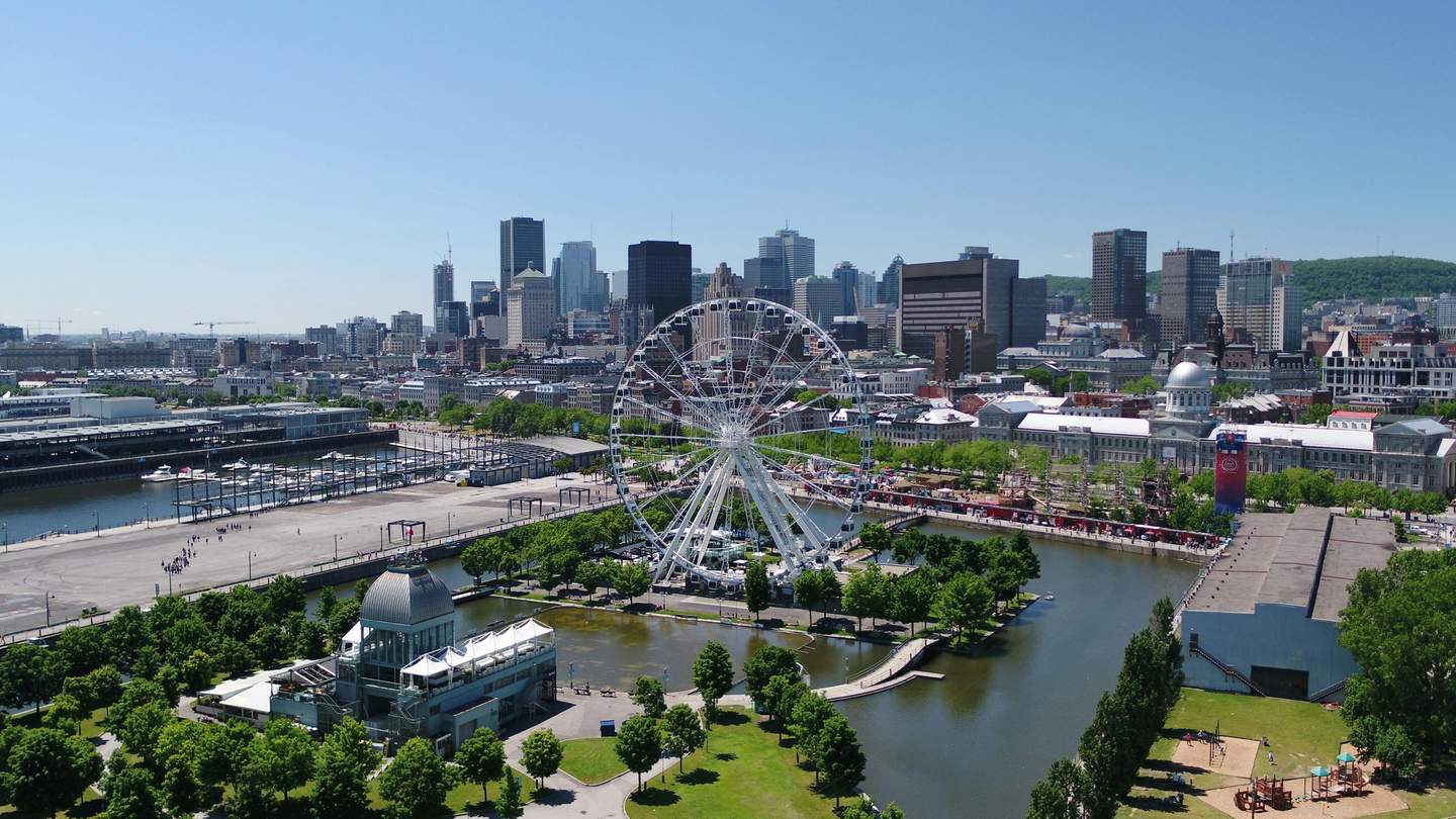 La Grande Roue de Montréal A Ferris wheel near water with city skyscrapers in the background, surrounded by trees, buildings, and recreational spaces.