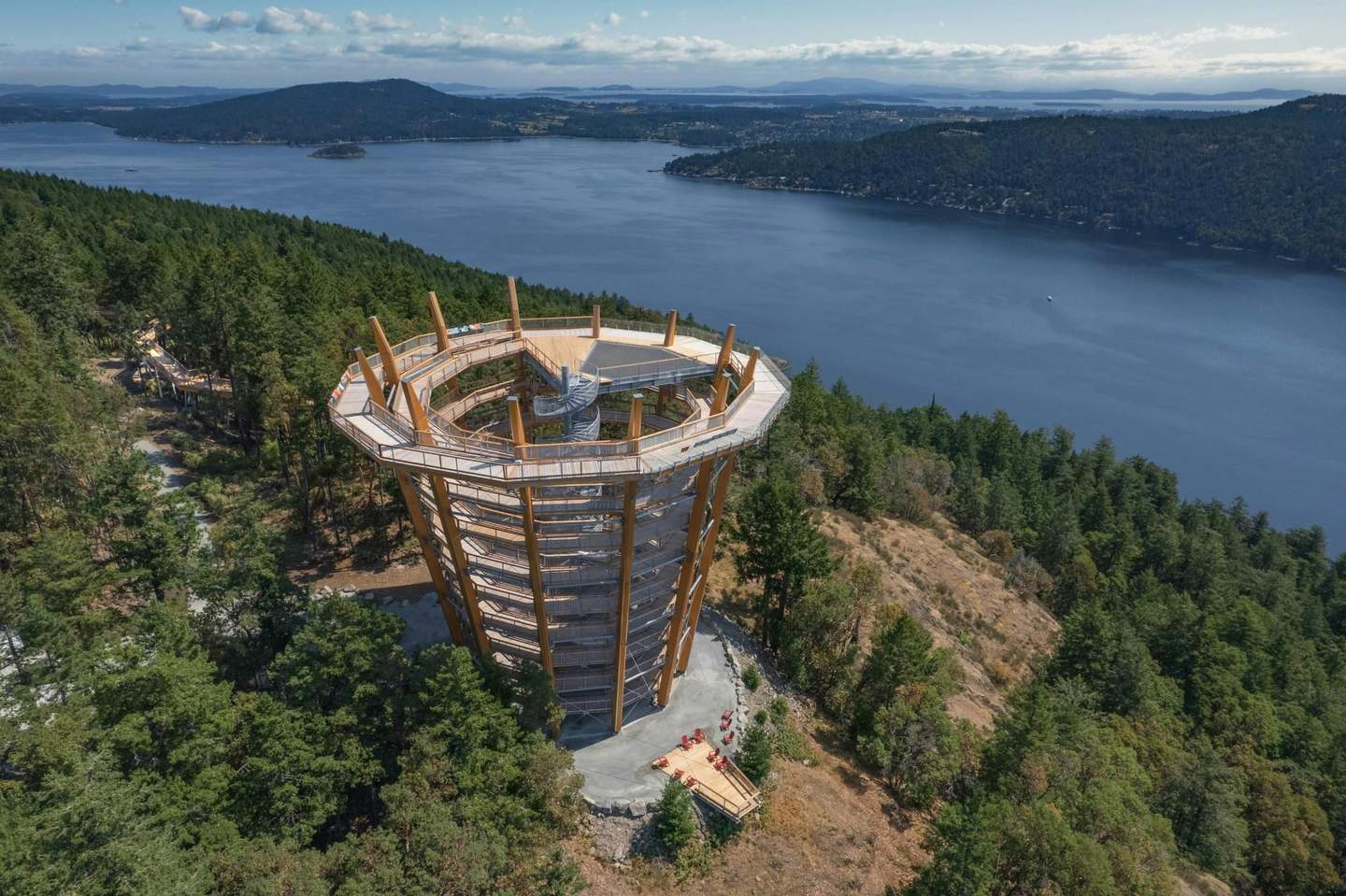 Malahat SkyWalk Observation tower with spiral walkway among dense trees, overlooking a serene body of water with hills in the distance.