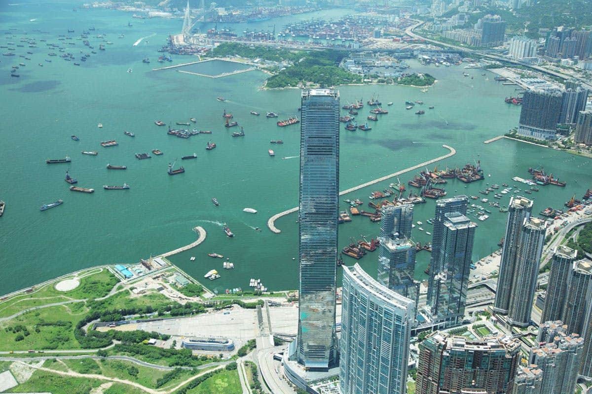 スカイ100香港展望台 高い高層ビル、緑豊かな港にある多数の船、広大な都市と緑のエリアがある沿岸都市の鳥瞰図。