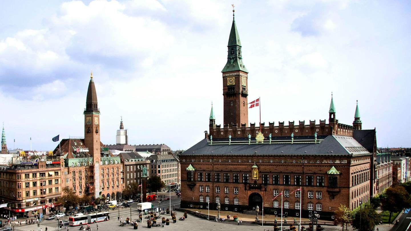 Copenhagen City Hall A large, ornate building with towers and a clock, Danish flags, busy street with buses and people, overcast sky.