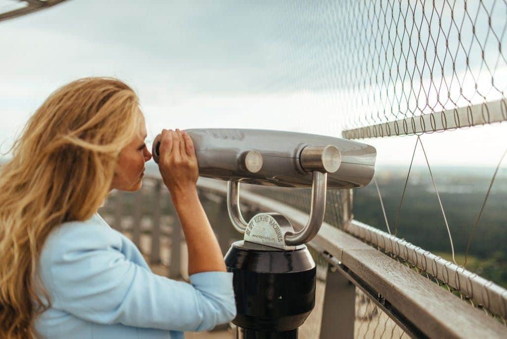 Tallinn TV Tower A person with long hair looks through a coin-operated binocular viewer on an outdoor observation deck.