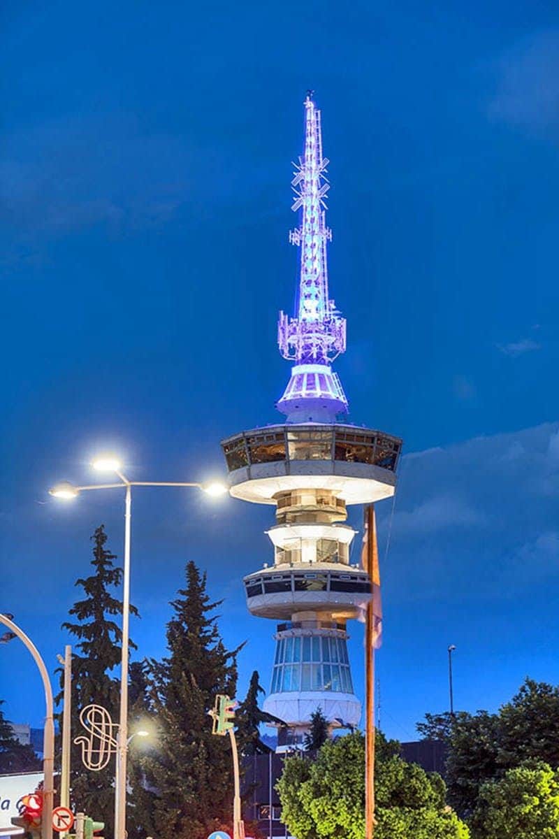 Skyline Cafe Bar - Dining A tall, modern tower illuminated with blue lights against a twilight sky, surrounded by trees and streetlights.