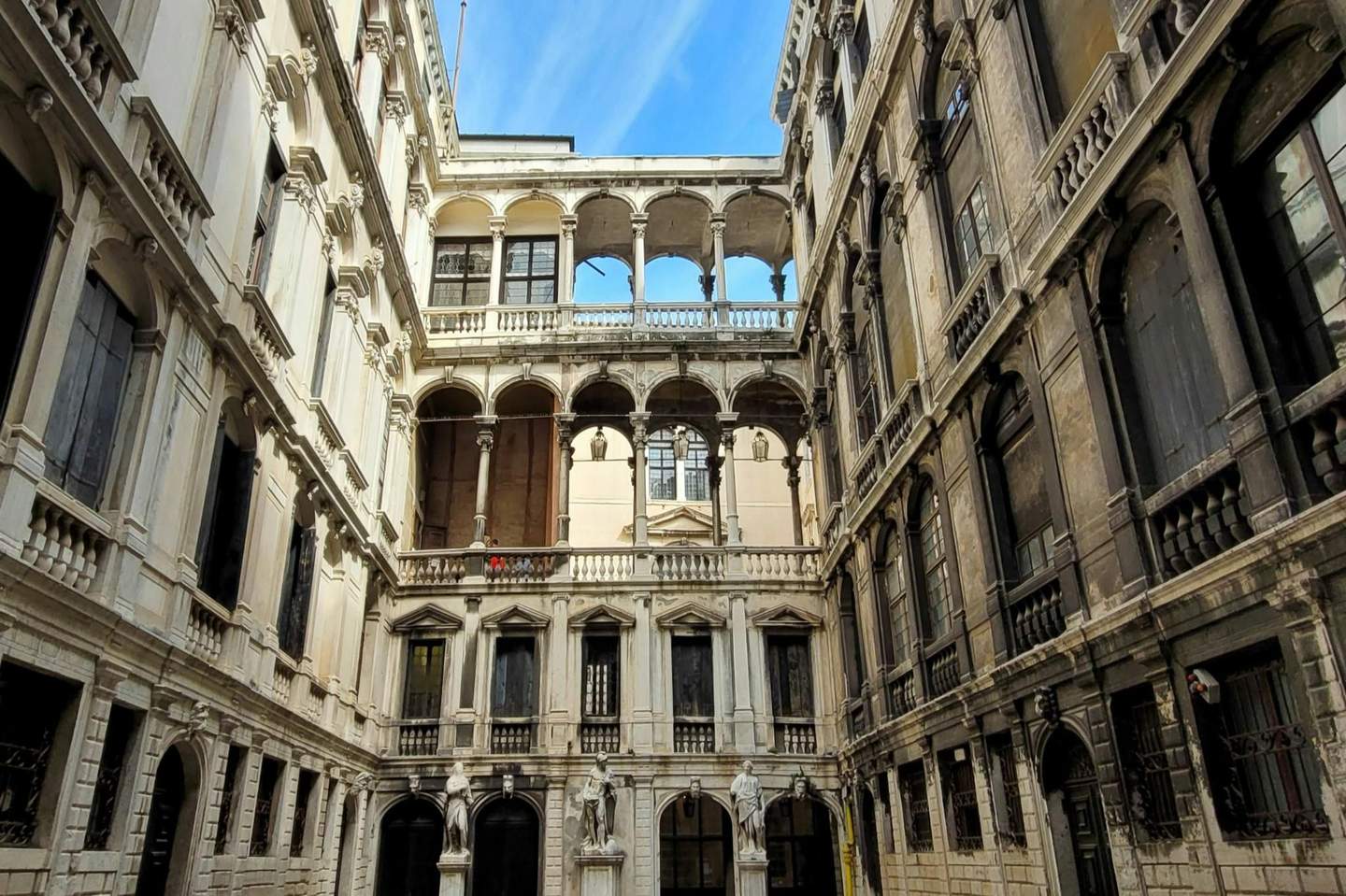 Palazzo Pisani A historic courtyard with ornate balconies, statues, arched windows, and a blue sky above.