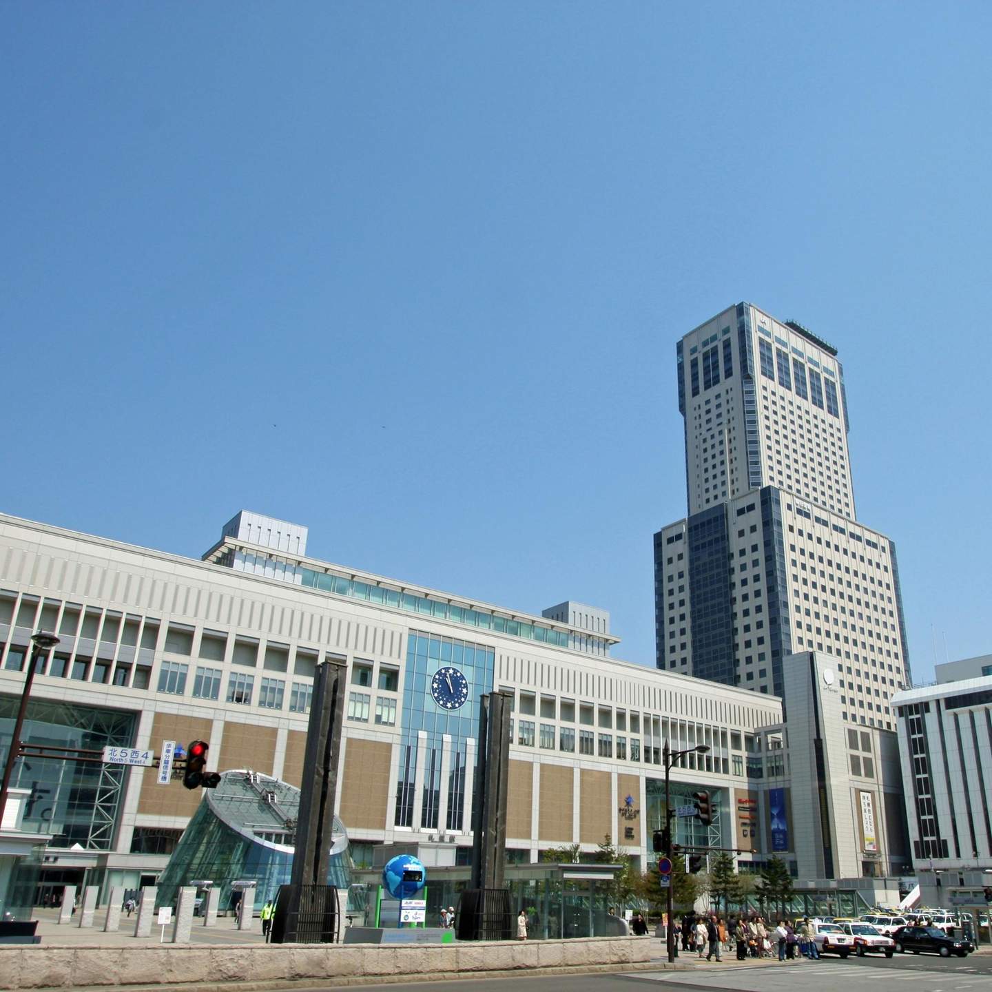 JR Tower Modern cityscape with a tall skyscraper and a multi-story building with a clock on the facade. Clear blue sky.