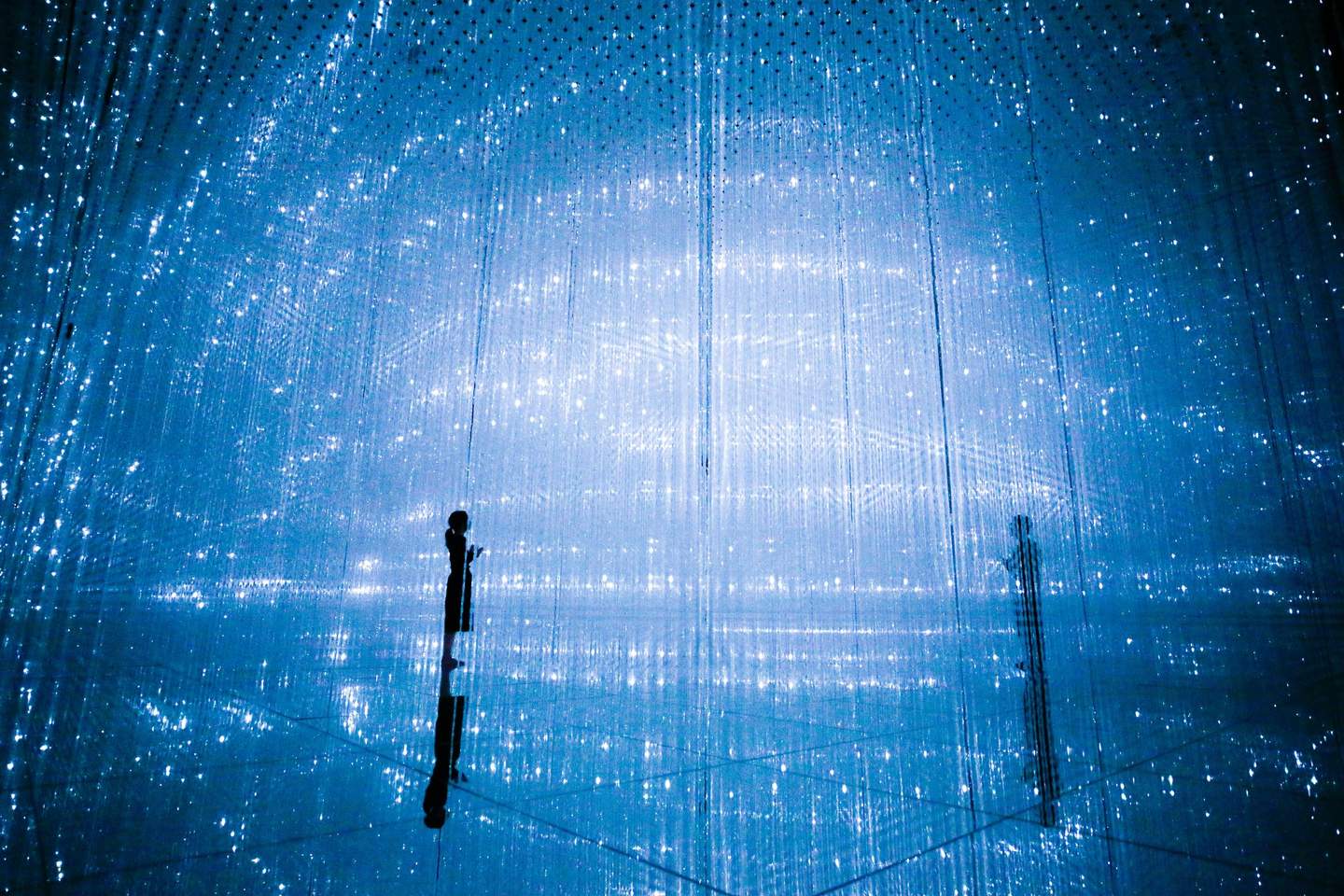 teamLab Planets Tokyo A silhouetted person stands amidst an immersive light installation with countless hanging blue LED lights.