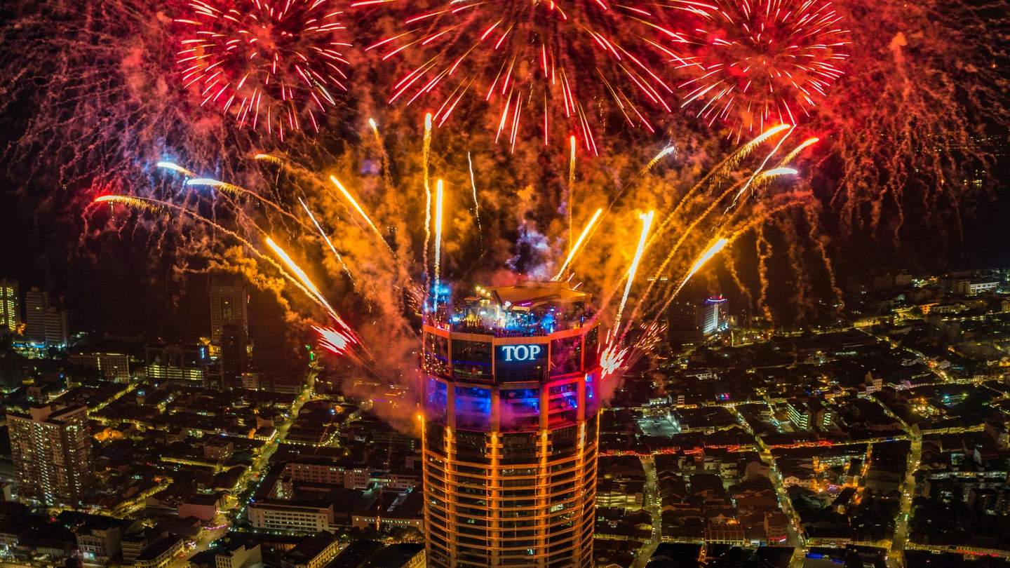 A tall building with a lit sign reading 'TOP' is surrounded by vibrant fireworks against a night cityscape.