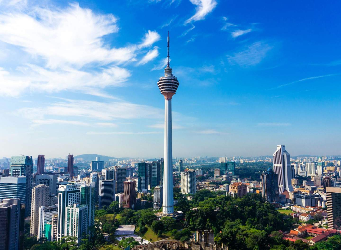 KL Tower A skyline with a tall observation tower surrounded by various modern buildings and green spaces under a bright blue sky.