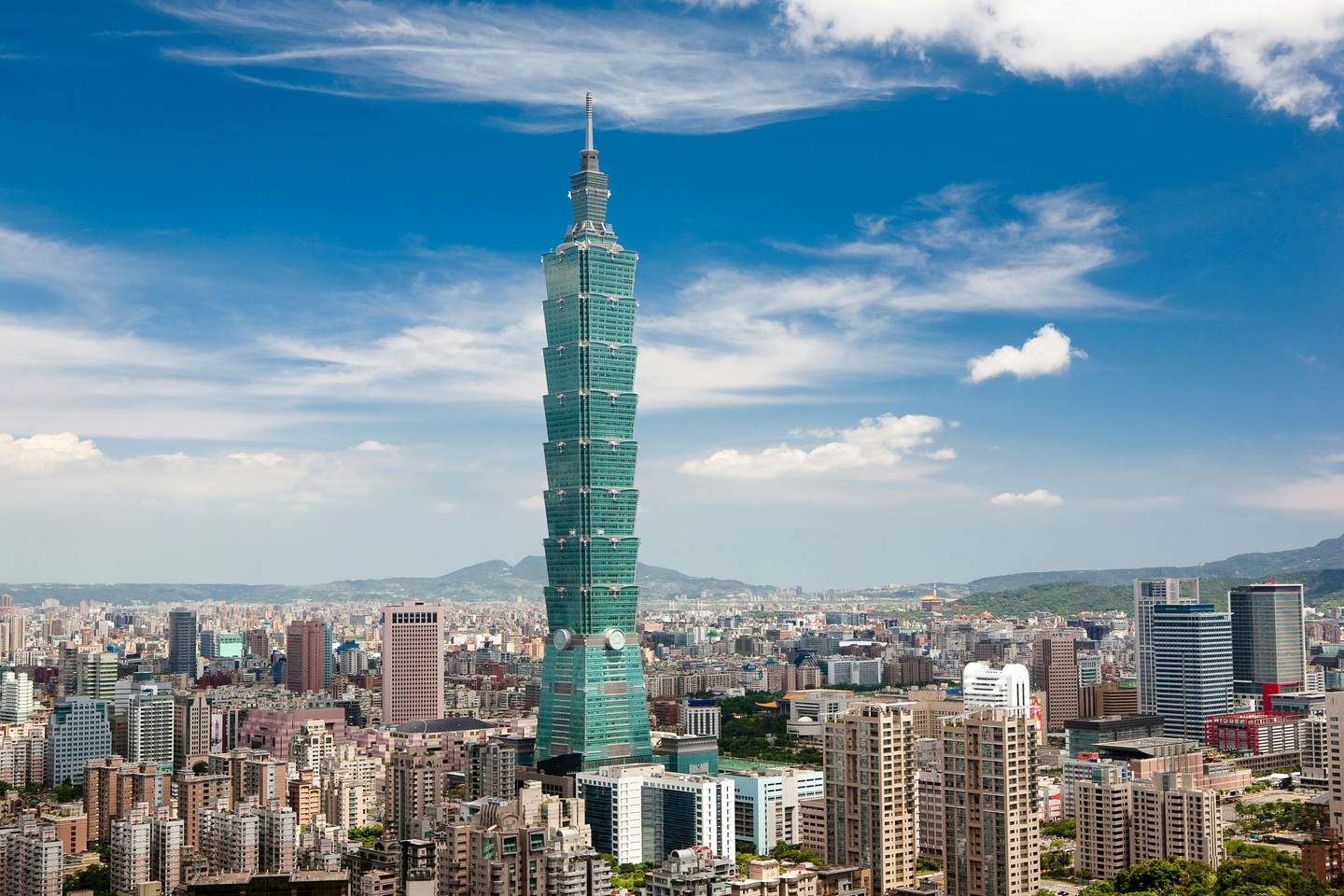 Taipei 101 A tall, tiered skyscraper stands prominently in a cityscape under a blue sky with scattered clouds.