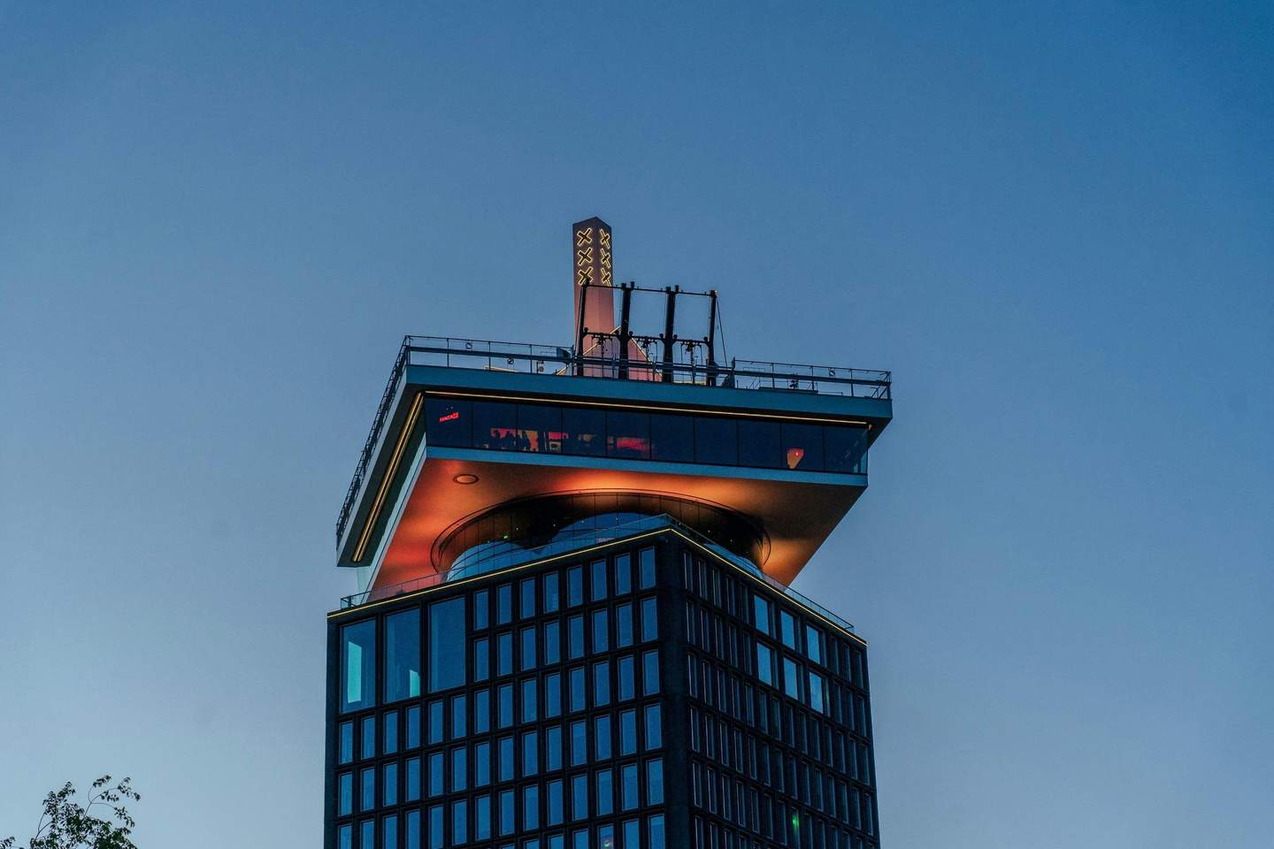 A'DAM Lookout A modern high-rise building with a rooftop observation deck and illuminated architectural features against a clear evening sky.