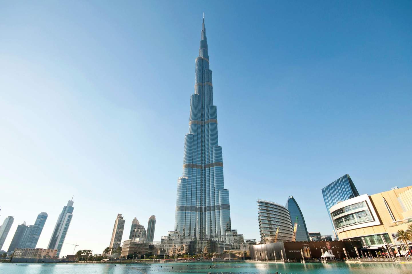 Burj Khalifa Tall skyscraper in a city with modern buildings and a reflecting pool in the foreground, under a clear blue sky.