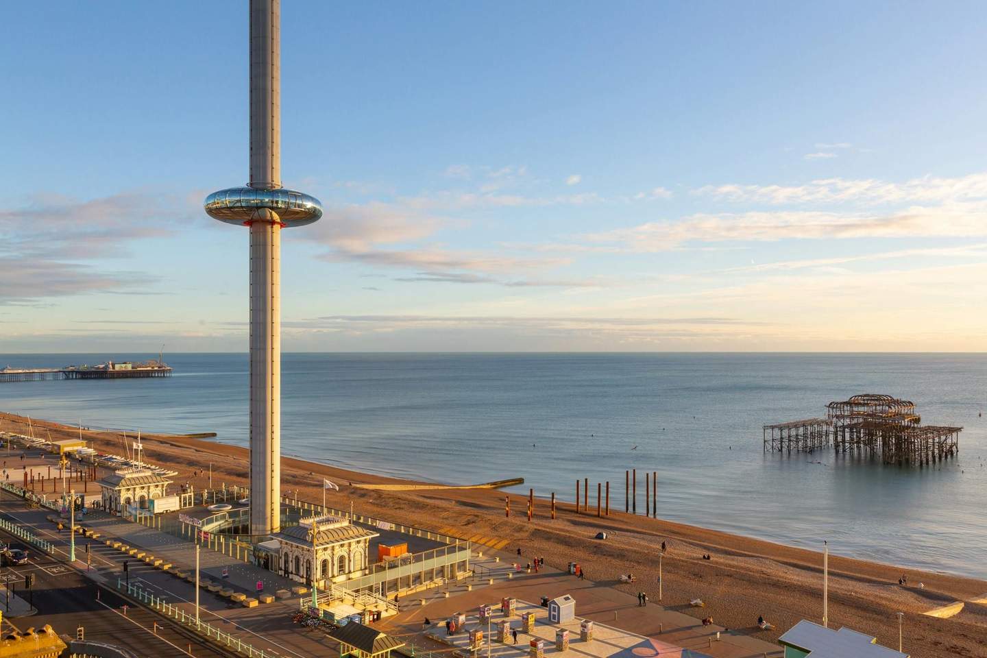 Brighton i360 Tall observation tower on a beach by the sea with a distant pier and the remains of an old structure in the water.