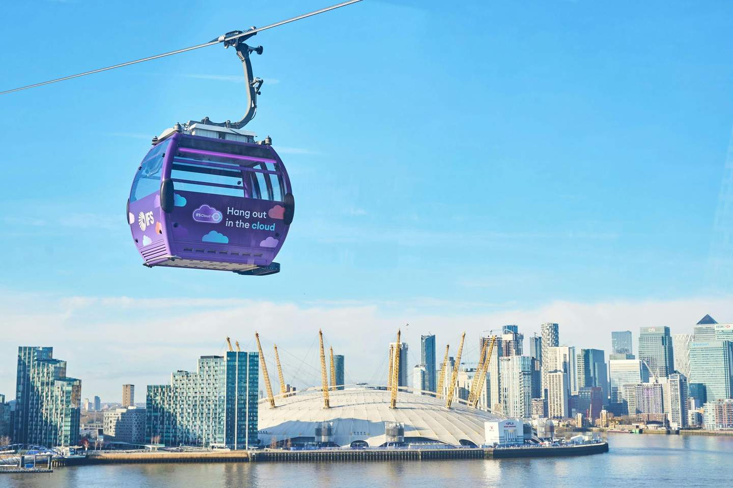 A purple cable car with text "Hang out in the cloud" moves above a city skyline featuring modern buildings and a dome.