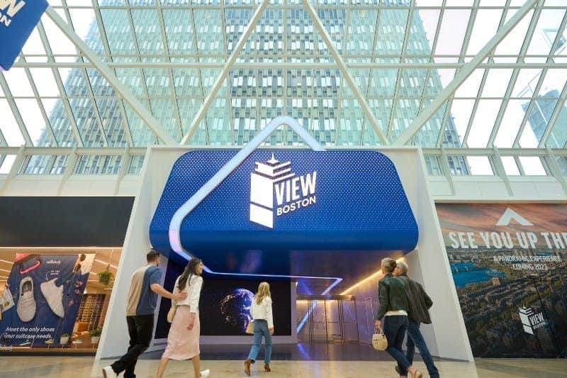 View Boston Observation Deck People walking in a modern, glass-covered atrium with a "View Boston" entrance, displaying an illuminated sign.