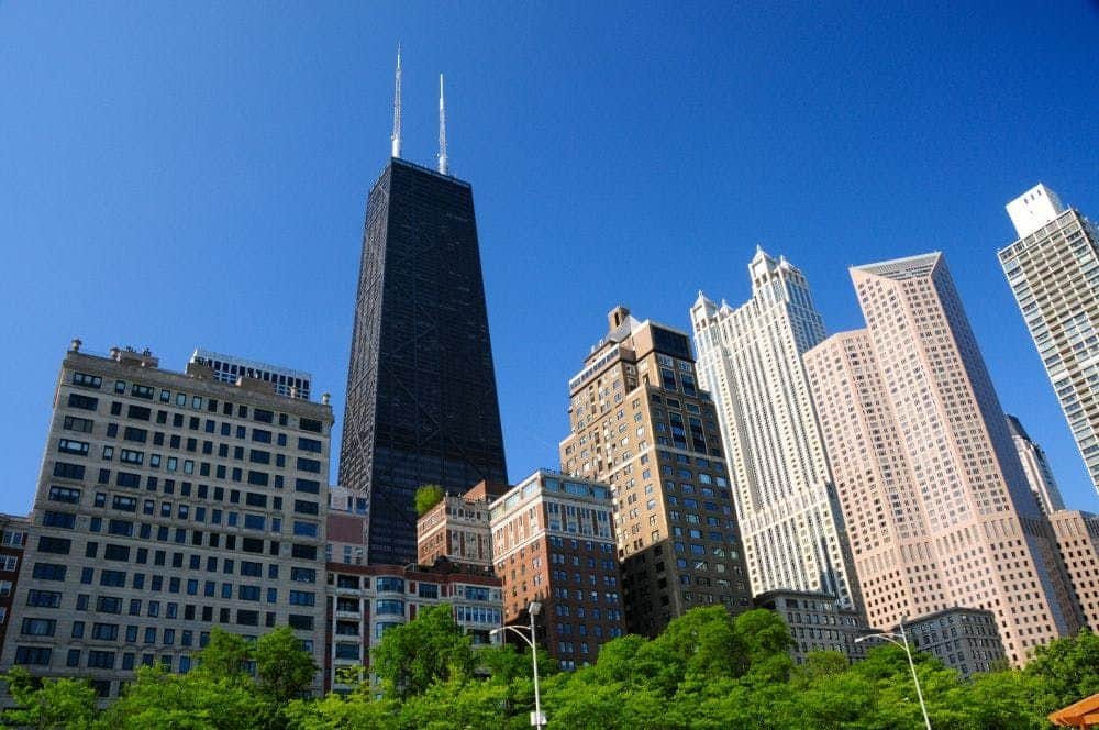 360 CHICAGO A skyline with various high-rise buildings against a clear blue sky, with trees in the foreground.